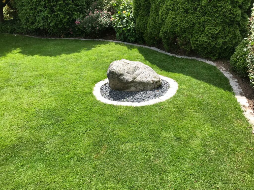 stor sten i midten af en grøn græsplæne i en have